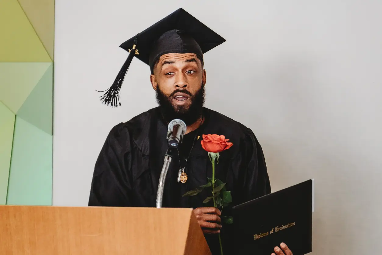 A man in graduation cap holding a rose.