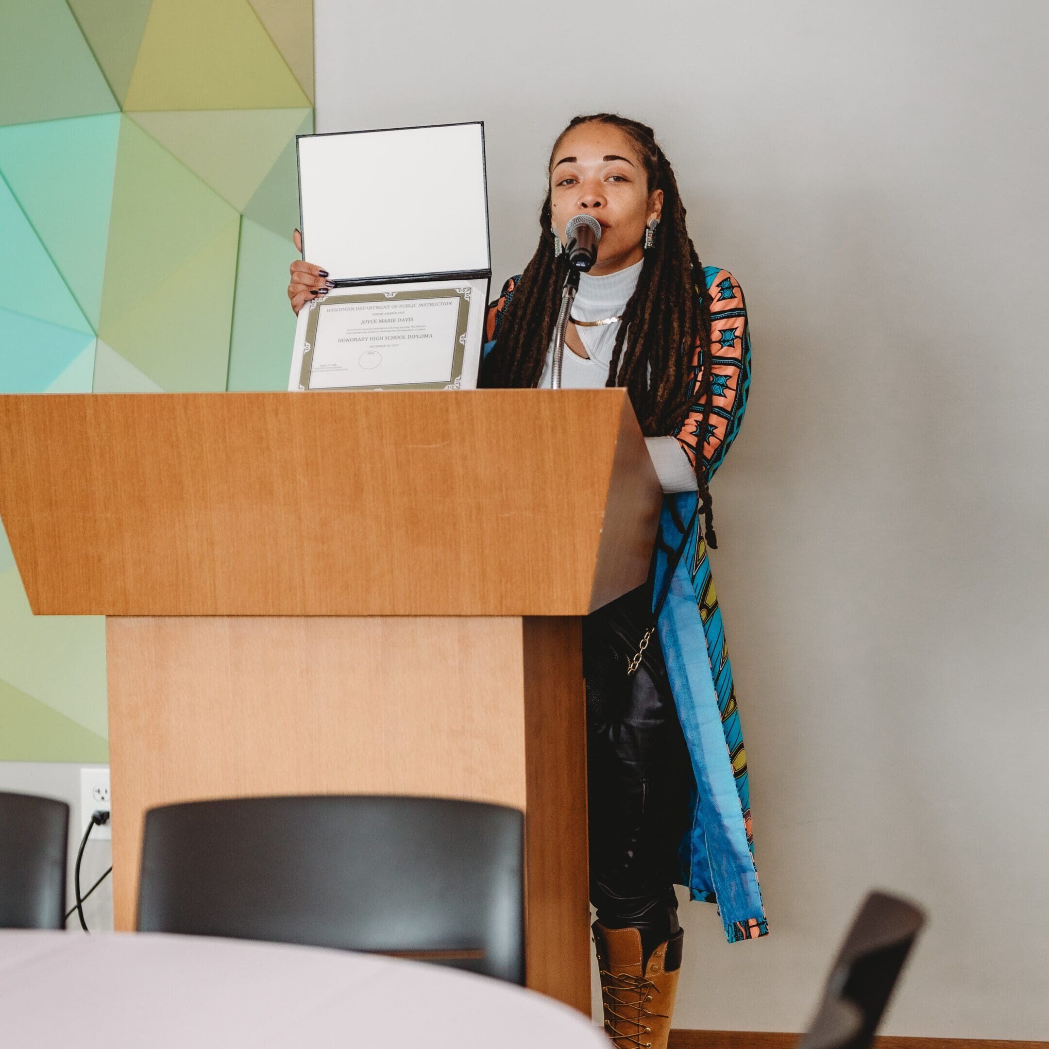 A woman standing at the top of a podium holding up a laptop.